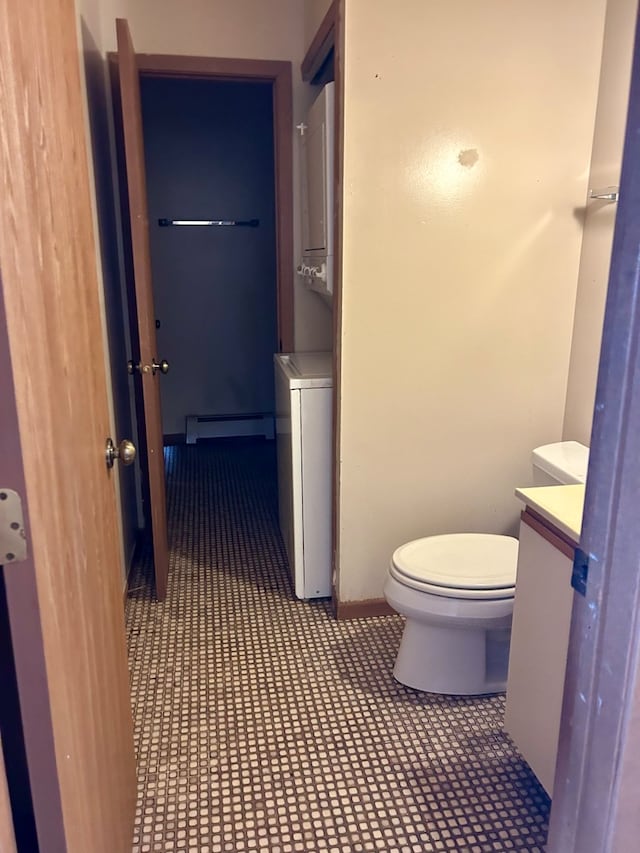 bathroom with stacked washer / dryer, vanity, toilet, and a baseboard radiator