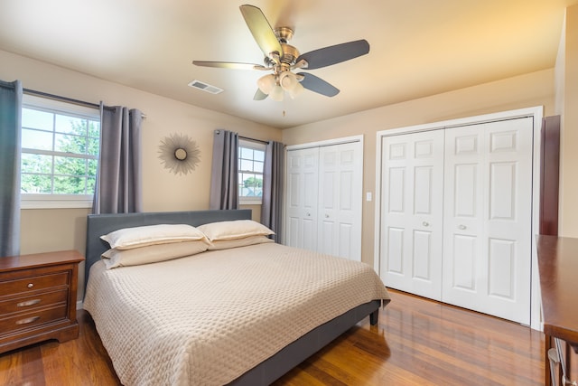 bedroom with two closets, wood-type flooring, and ceiling fan