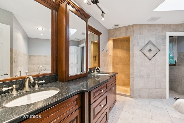 bathroom featuring track lighting, tile patterned flooring, vanity, tiled shower, and tile walls