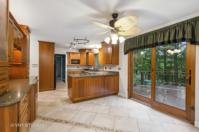 kitchen featuring stainless steel gas stovetop, kitchen peninsula, ceiling fan, black microwave, and light tile patterned flooring