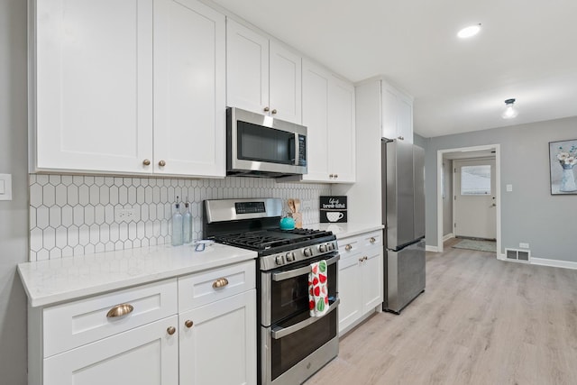 kitchen with white cabinetry, light hardwood / wood-style flooring, appliances with stainless steel finishes, light stone countertops, and backsplash