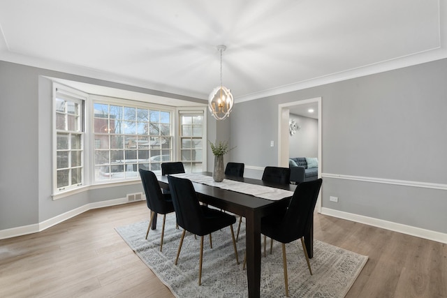 dining area with ornamental molding, a chandelier, and light hardwood / wood-style flooring