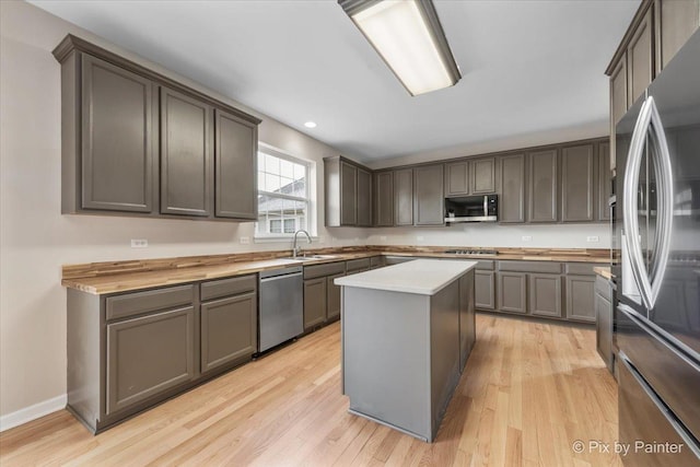 kitchen with wooden counters, sink, light hardwood / wood-style flooring, appliances with stainless steel finishes, and a kitchen island