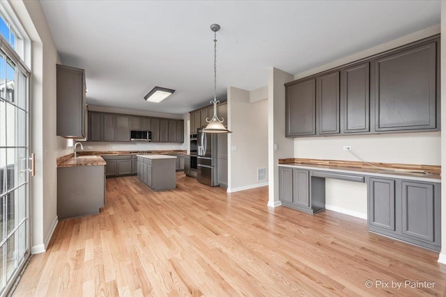 kitchen featuring sink, a center island, decorative light fixtures, gray cabinets, and light wood-type flooring