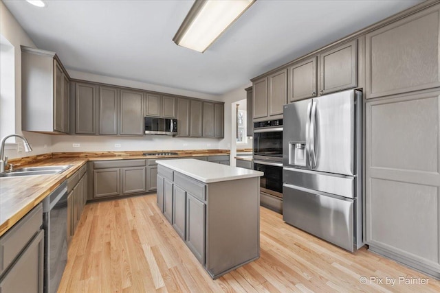 kitchen with appliances with stainless steel finishes, gray cabinetry, sink, light hardwood / wood-style floors, and a kitchen island