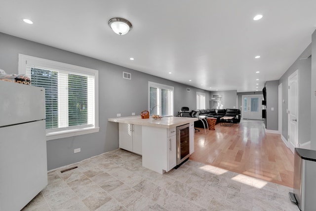 kitchen with beverage cooler, white refrigerator, light wood-type flooring, and white cabinets