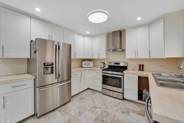 kitchen with wall chimney exhaust hood, white cabinetry, stainless steel appliances, and sink