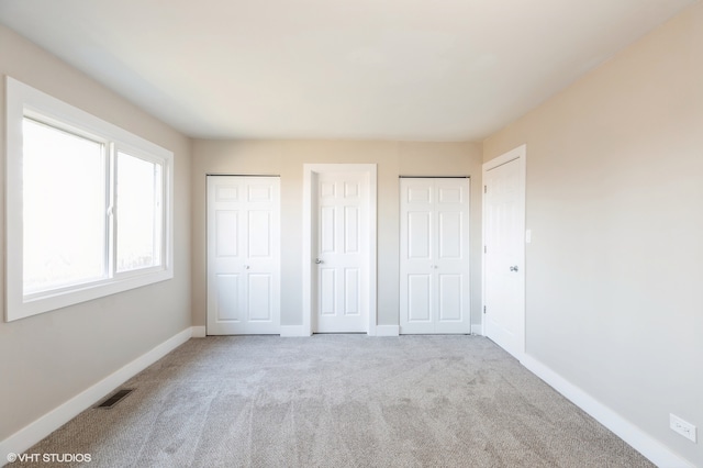 unfurnished bedroom with light carpet and two closets