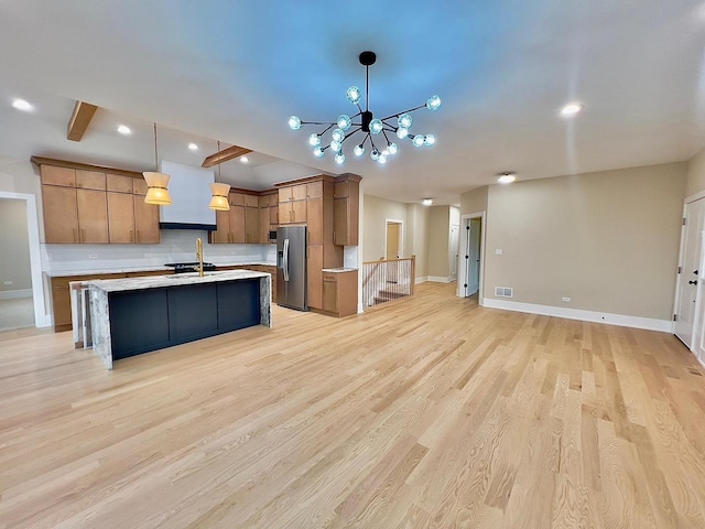 kitchen with tasteful backsplash, stainless steel refrigerator with ice dispenser, an island with sink, decorative light fixtures, and light wood-type flooring