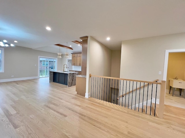 kitchen featuring pendant lighting, light hardwood / wood-style floors, sink, and an island with sink