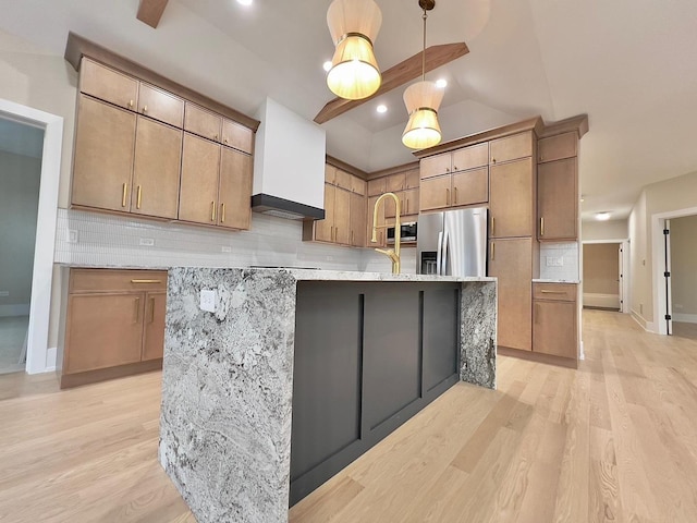 kitchen featuring appliances with stainless steel finishes, tasteful backsplash, a kitchen island with sink, light hardwood / wood-style floors, and hanging light fixtures