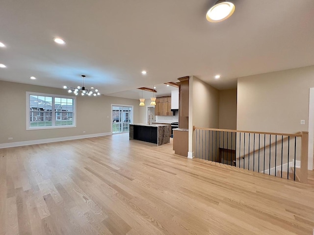 unfurnished living room with light hardwood / wood-style floors, sink, and a chandelier