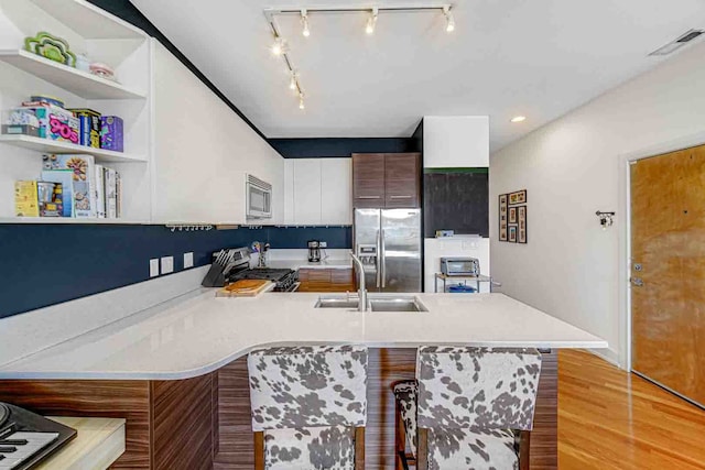 kitchen featuring light hardwood / wood-style floors, a kitchen bar, kitchen peninsula, sink, and stainless steel appliances