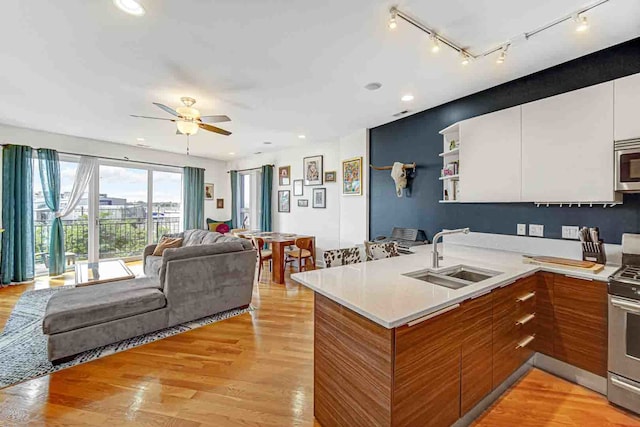 kitchen with light wood-type flooring, white cabinetry, stainless steel appliances, sink, and ceiling fan