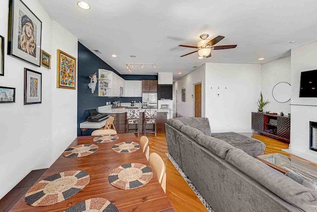 living room with light wood-type flooring, track lighting, and ceiling fan