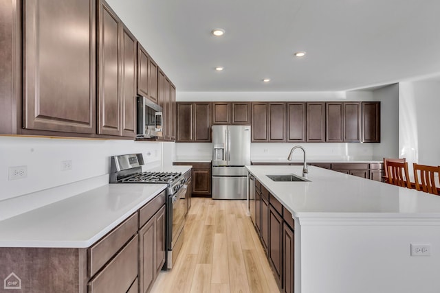 kitchen featuring light wood-type flooring, appliances with stainless steel finishes, a kitchen island with sink, sink, and dark brown cabinetry