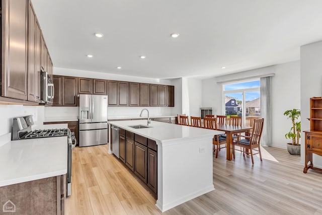 kitchen with appliances with stainless steel finishes, light hardwood / wood-style floors, an island with sink, and sink