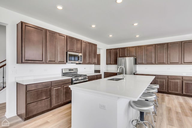 kitchen with a kitchen island with sink, light hardwood / wood-style flooring, a kitchen bar, and stainless steel appliances