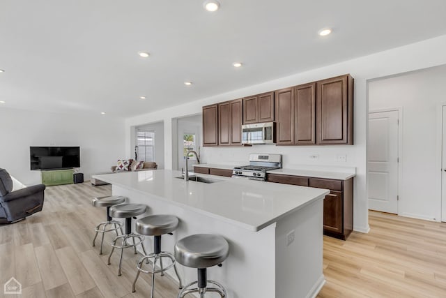 kitchen with stainless steel appliances, sink, a breakfast bar area, a center island with sink, and light hardwood / wood-style floors