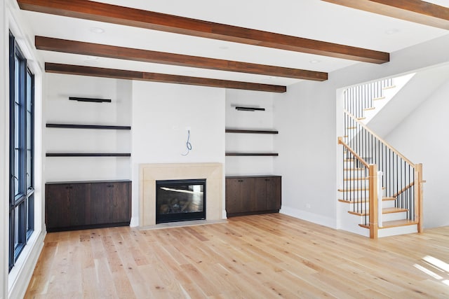 unfurnished living room featuring plenty of natural light, a premium fireplace, light hardwood / wood-style flooring, and built in shelves