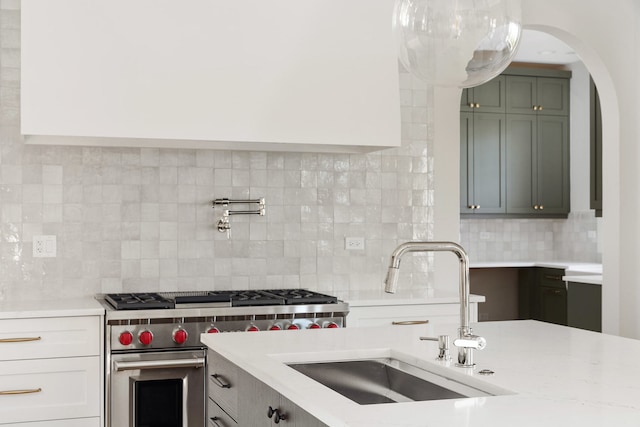 kitchen featuring light stone countertops, luxury stove, sink, and decorative backsplash