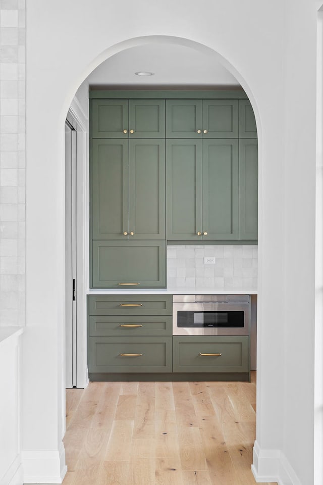 bar featuring tasteful backsplash, green cabinets, and light hardwood / wood-style floors