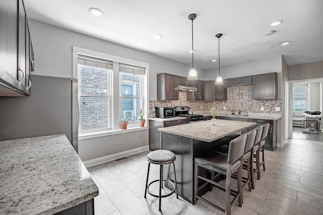 kitchen with light stone countertops, appliances with stainless steel finishes, a kitchen bar, a center island, and decorative backsplash