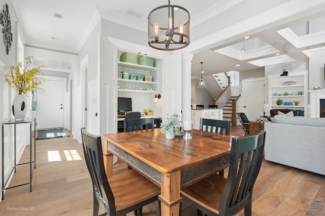 dining room featuring ornamental molding, light wood-type flooring, a chandelier, and ornate columns