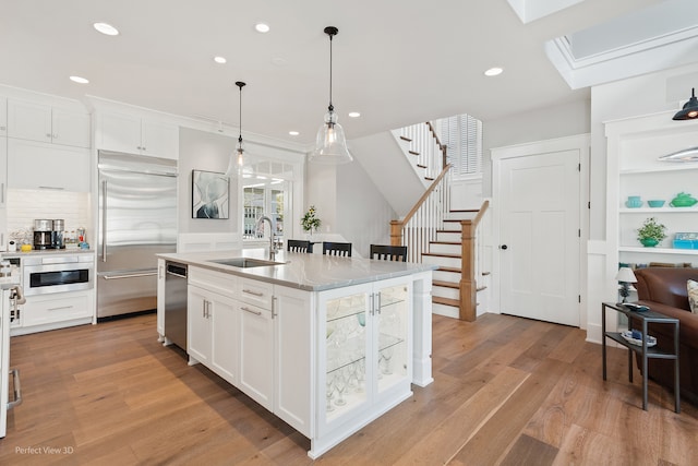 kitchen with a kitchen island with sink, light hardwood / wood-style flooring, stainless steel appliances, sink, and white cabinets