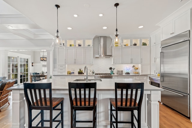 kitchen with wall chimney exhaust hood, light hardwood / wood-style flooring, a large island with sink, and appliances with stainless steel finishes