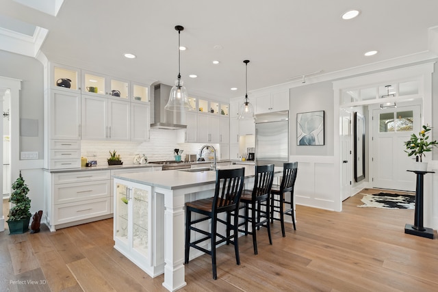 kitchen featuring white cabinets, light hardwood / wood-style flooring, sink, wall chimney exhaust hood, and a kitchen island with sink