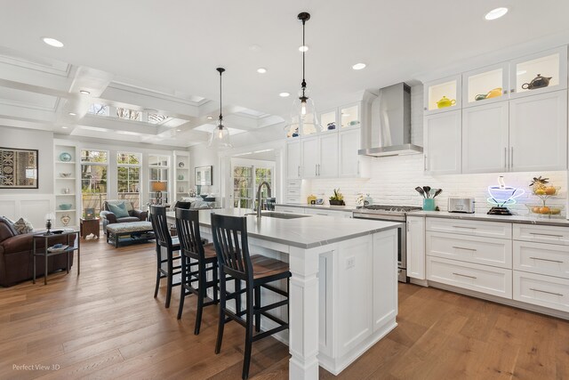 kitchen with wall chimney range hood, white cabinets, stainless steel gas stove, and a kitchen island with sink