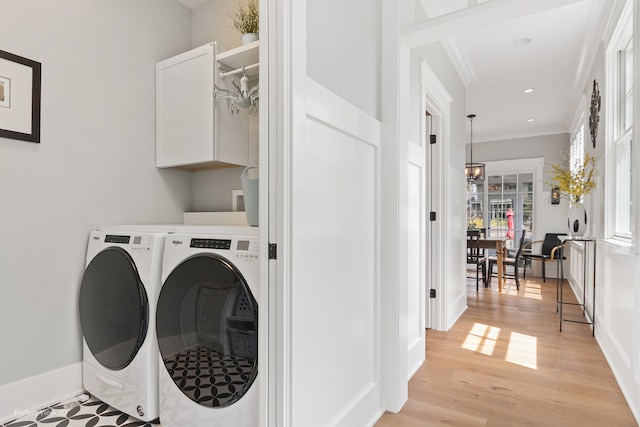 clothes washing area featuring light wood-type flooring, crown molding, independent washer and dryer, and cabinets