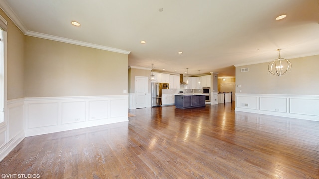 unfurnished living room featuring wood-type flooring, an inviting chandelier, and crown molding