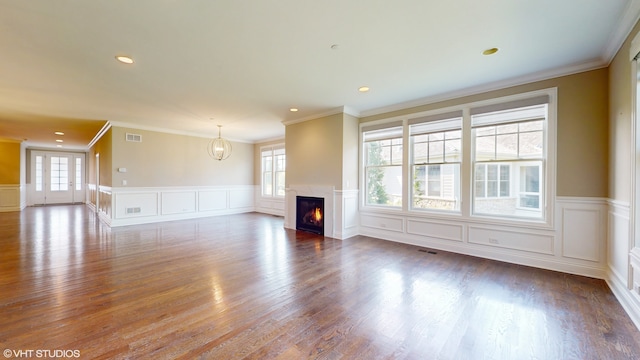 unfurnished living room with a healthy amount of sunlight, ornamental molding, and wood-type flooring