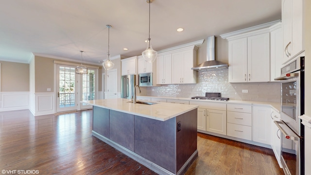 kitchen featuring crown molding, sink, wall chimney exhaust hood, appliances with stainless steel finishes, and a center island with sink