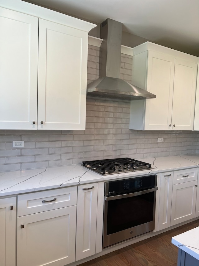 kitchen with light stone counters, dark hardwood / wood-style floors, appliances with stainless steel finishes, white cabinets, and wall chimney range hood