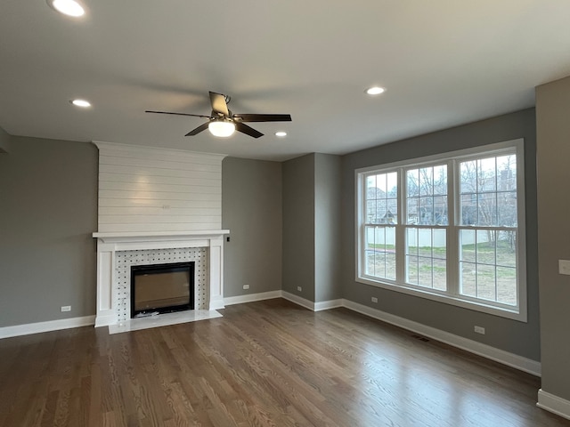 unfurnished living room featuring ceiling fan, a tiled fireplace, and wood-type flooring