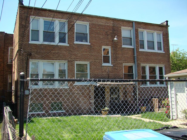 back of property featuring fence, a lawn, and brick siding