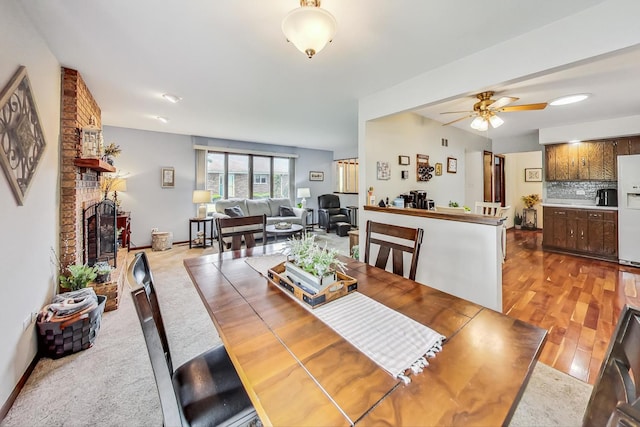 dining space featuring ceiling fan, a fireplace, and light hardwood / wood-style flooring