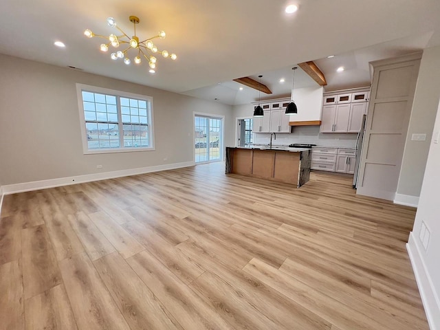 kitchen with beam ceiling, sink, hanging light fixtures, light hardwood / wood-style flooring, and a large island with sink