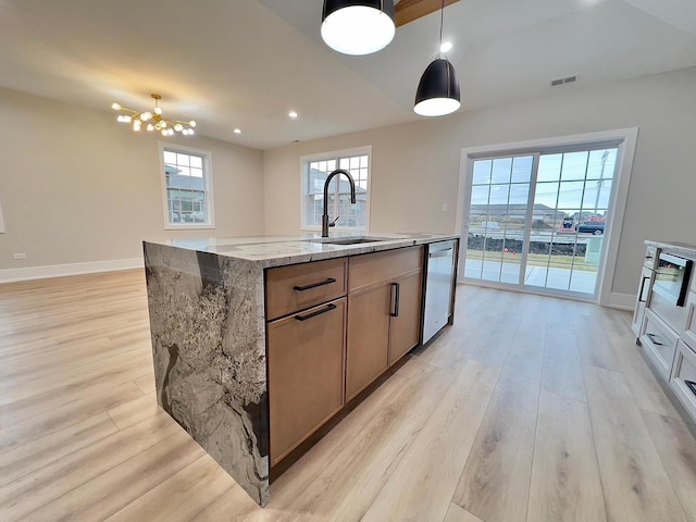 kitchen featuring light stone countertops, a kitchen island with sink, sink, pendant lighting, and light hardwood / wood-style floors