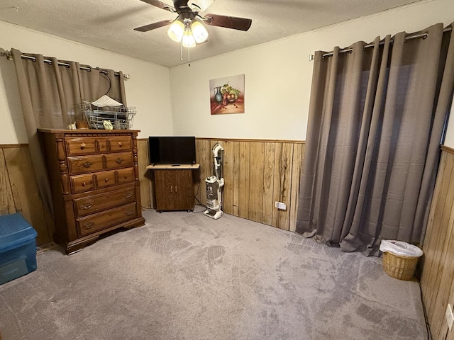 carpeted bedroom with a textured ceiling, wooden walls, and ceiling fan