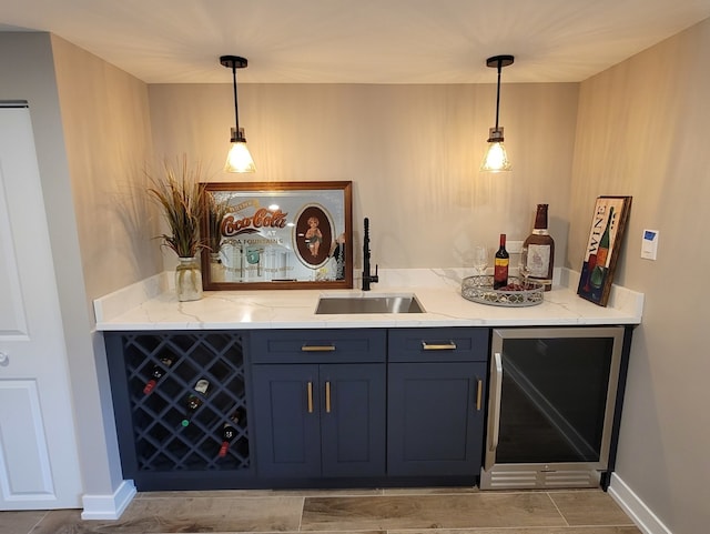 bar with decorative light fixtures, light stone counters, sink, beverage cooler, and blue cabinets