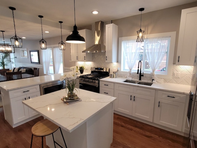 kitchen with wall chimney range hood, appliances with stainless steel finishes, decorative light fixtures, and sink