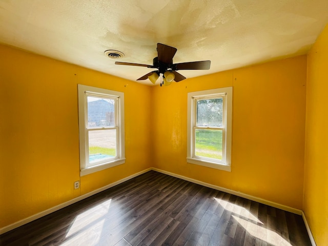 unfurnished room featuring dark wood-type flooring, a textured ceiling, a wealth of natural light, and ceiling fan