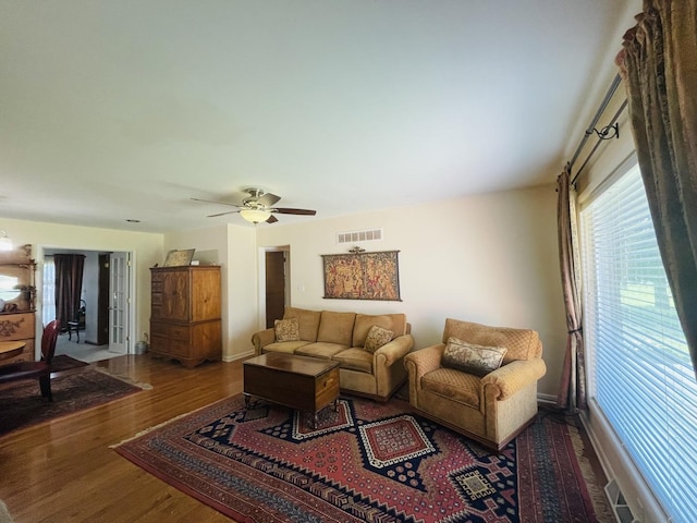 living room featuring a ceiling fan, visible vents, baseboards, and wood finished floors