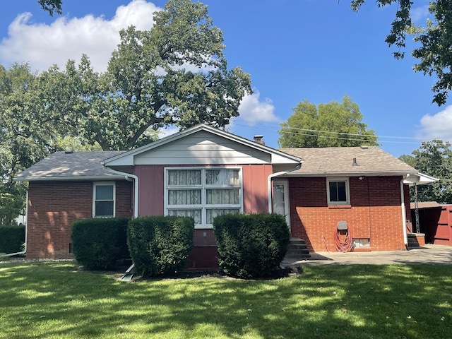 view of front facade featuring brick siding, a chimney, a front yard, and a shingled roof