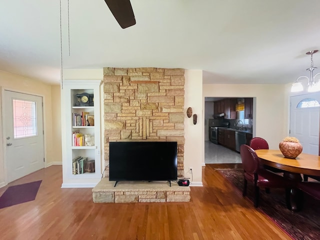 living room featuring built in shelves, a notable chandelier, sink, a stone fireplace, and hardwood / wood-style flooring