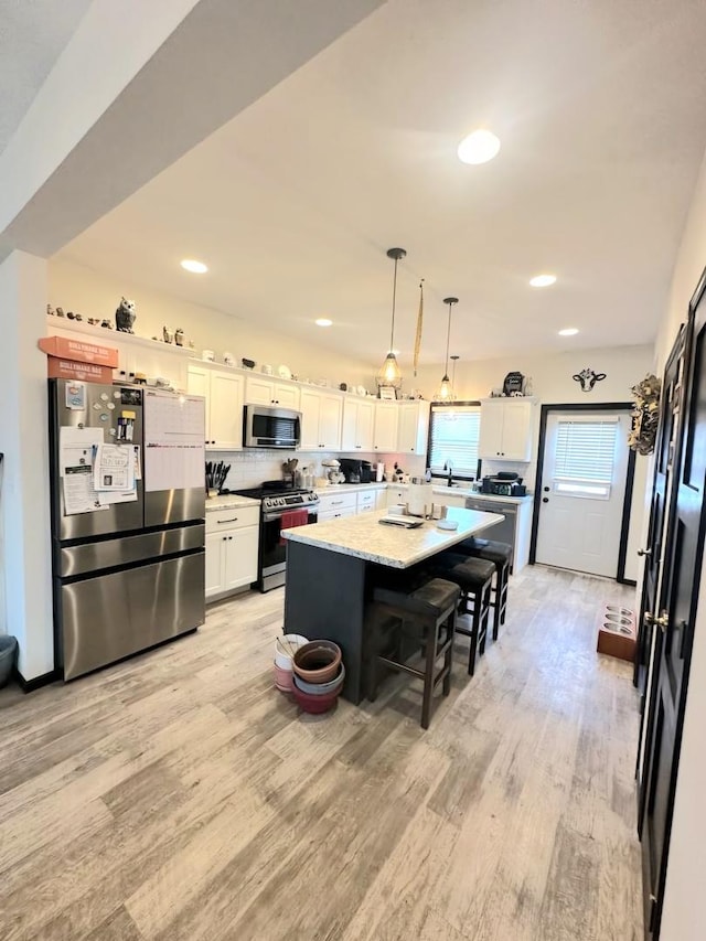 kitchen with a breakfast bar, white cabinetry, appliances with stainless steel finishes, a center island, and light wood finished floors